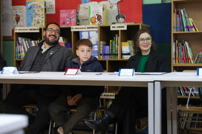 Ministra Vallejo y ministro Cataldo junto a estudiante la escuela Alexander Graham Bell de Pudahuel, sentados en una biblioteca para el lanzamiento del plan de Ciudadanía Digital